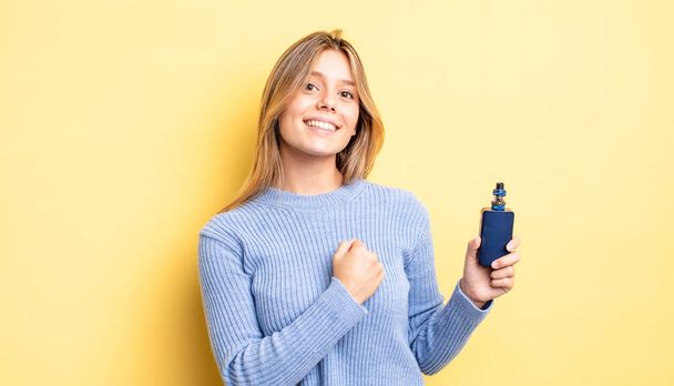pretty blonde girl feeling happy and facing a challenge or celebrating. smoke vaporizer concept - Foto, afbeelding