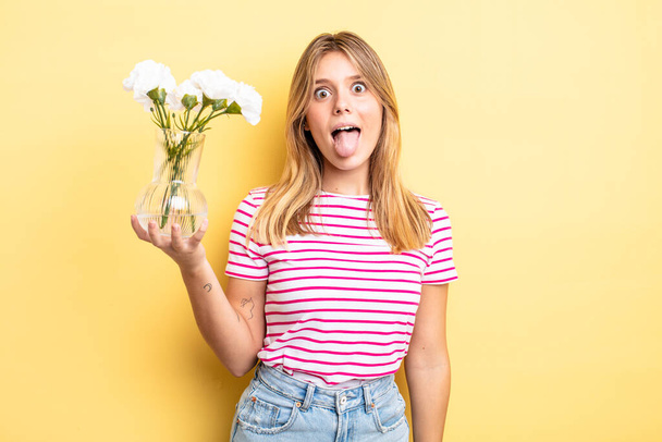 pretty blonde girl with cheerful and rebellious attitude, joking and sticking tongue out. decorative flowers concept - 写真・画像