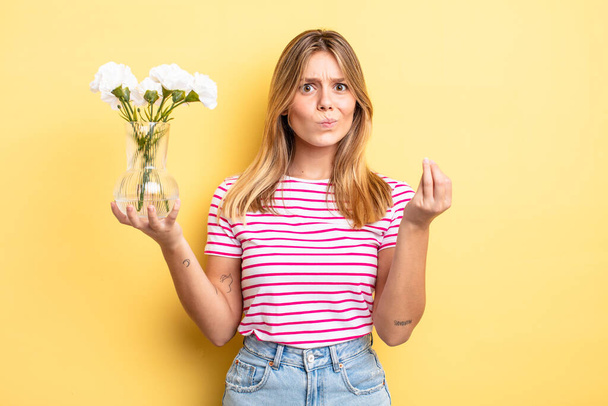 pretty blonde girl making capice or money gesture, telling you to pay. decorative flowers concept - Фото, зображення