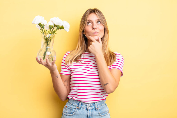 pretty blonde girl thinking, feeling doubtful and confused. decorative flowers concept - Photo, image