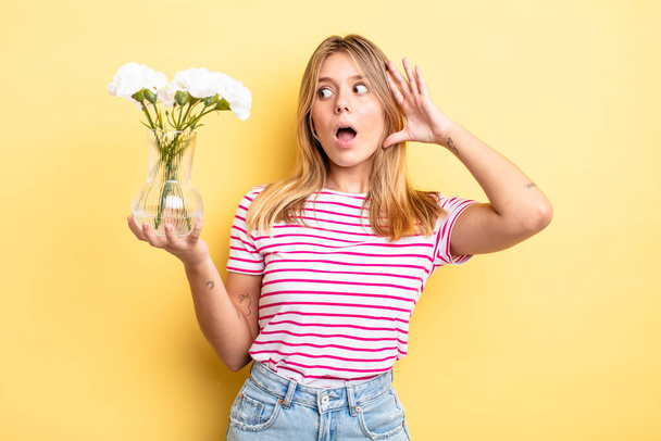 pretty blonde girl feeling happy, excited and surprised. decorative flowers concept - Foto, Bild