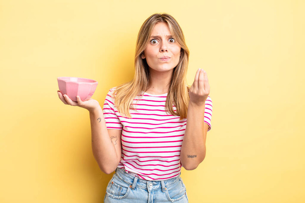 pretty blonde girl making capice or money gesture, telling you to pay. empty bowl concept - 写真・画像
