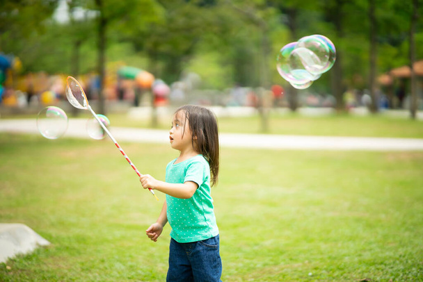 Kedves aktív kis ázsiai lány játszik szappanbuborék szabadban a parkban - Fotó, kép