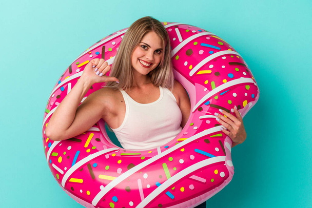 jonge russische vrouw met opblaasbare donut geïsoleerd op blauwe achtergrond voelt trots en zelfverzekerd, voorbeeld te volgen. - Foto, afbeelding