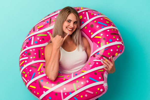 Young russian woman with inflatable donut isolated on blue background showing a mobile phone call gesture with fingers. - Foto, Imagen