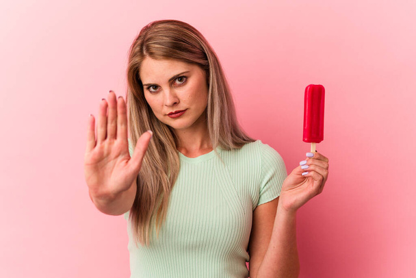Молодая россиянка, держащая мороженое на розовом фоне, стоящая с протянутой рукой, показывая знак "стоп", препятствуя вам. - Фото, изображение