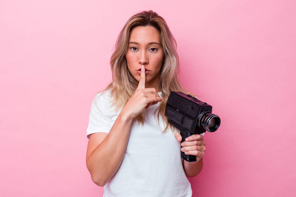 Young australian woman filming with a vintage video camera isolated keeping a secret or asking for silence. - Photo, Image