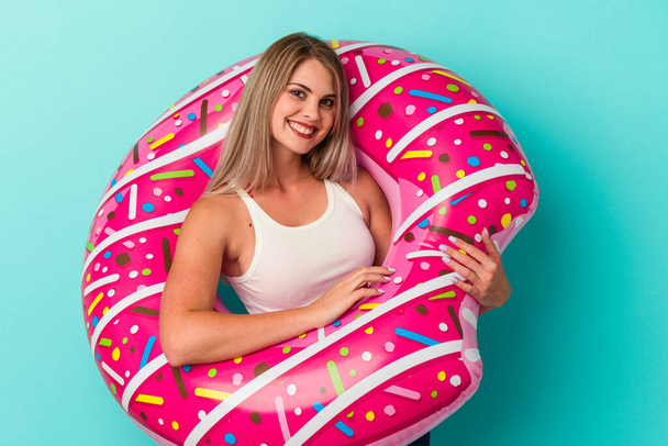 Young russian woman with inflatable donut isolated on blue background happy, smiling and cheerful. - Photo, Image