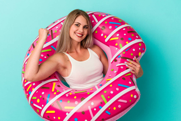 Young russian woman with inflatable donut isolated on blue background raising fist after a victory, winner concept. - Fotografie, Obrázek