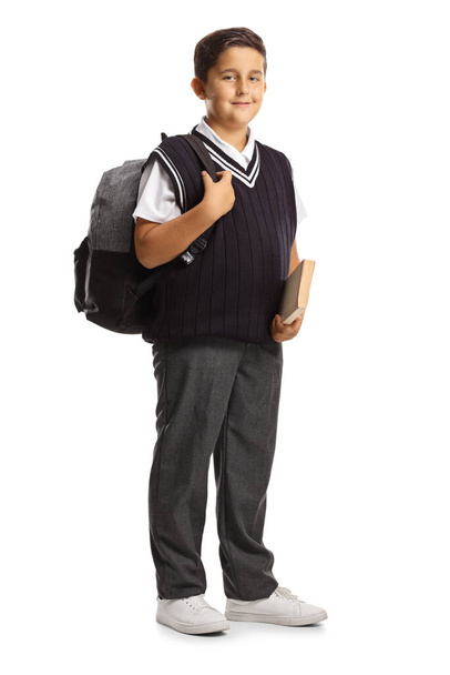 Πλήρες πορτραίτο ενός άνδρα μαθητή με σχολική στολή που κρατάει ένα βιβλίο και κουβαλάει ένα σακίδιο που είναι απομονωμένο σε λευκό φόντο - Φωτογραφία, εικόνα