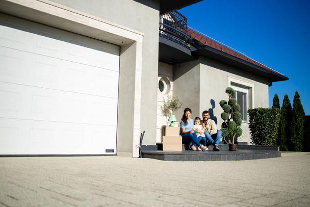 Portrait de famille caucasienne heureuse assise sur le porche de leur nouvelle maison prête à emménager. - Photo, image