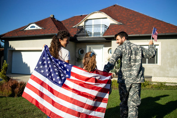 アメリカ国旗を掲揚し、父兵士を家に迎え入れる幸せな軍事家族. - 写真・画像