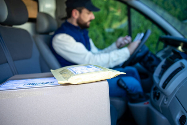 Close up view on package shipment and delivery man driver filling papers in his van. - Photo, Image