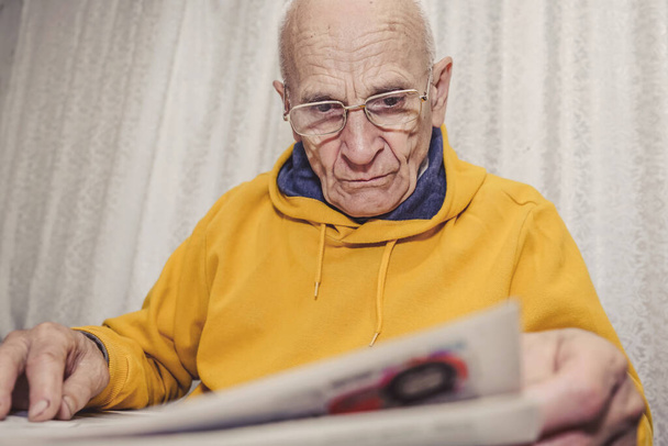 Aged grandpa with wrinkled face reading newspaper sitting at table - Photo, image