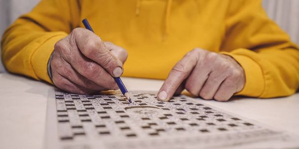 Male wrinkled hand holding blue pencil and writing letter in crossword - Foto, immagini
