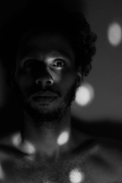 Portrait of a man. bare chest. in the dark. looking the camera. low light. black and white - Фото, изображение