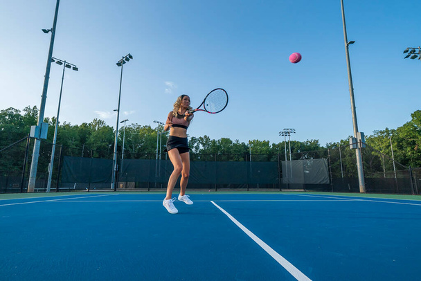 A gorgeous blonde model plays tennis in the afternoon sun on a tennis court - Photo, Image