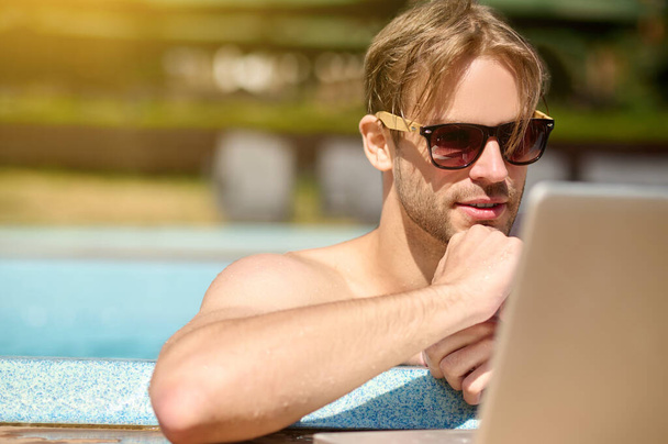 Молодий чоловік проводить час у басейні і дивиться щось онлайн
 - Фото, зображення