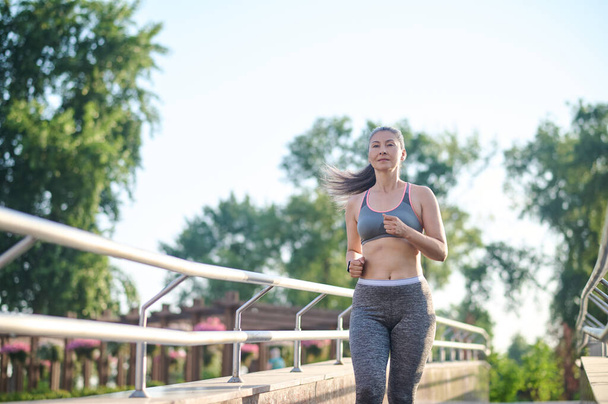 A woman in grey sportswear jogging in the park - Фото, зображення