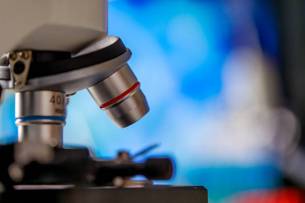 Σύγχρονο επιστημονικό μικροσκόπιο με τρεις στόχους επιλεκτικού φακού για διάφορες μεγεθύνσεις ή παρατήρηση με μεγέθυνση που χρησιμοποιείται ως μικροβιολογική συσκευή στο εργαστήριο χημείας για την μπλε παθογόνο υγρή διάγνωση - Φωτογραφία, εικόνα