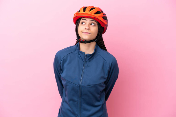 tiener fietser meisje geïsoleerd op roze achtergrond en op zoek omhoog - Foto, afbeelding