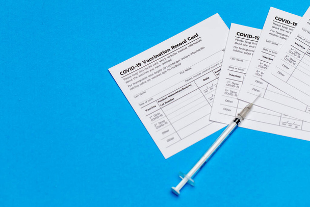 Medical syringe and covid-19 vaccination record cards prepared at healthcare clinic for doctor to note patient info, dose, date as measure to activate social immunity against outbreak - Фото, изображение