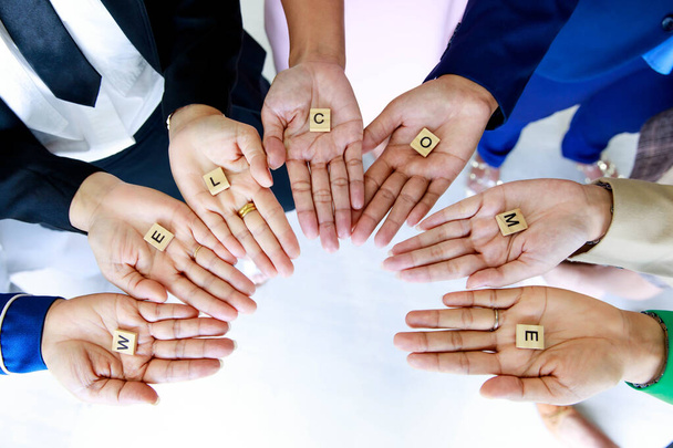 Studyjne ujęcie małych drewnianych sześcianów bloku powitalnego litery alfabetów trzymać w rękach przez nierozpoznawalny niezidentyfikowany personel oficer w ubraniach biznesowych pokazać ciepłe pozdrowienia dla klientów lub kolegów. - Zdjęcie, obraz