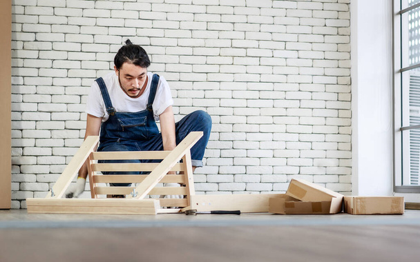Молодой человек азиатский хипстер работает разнорабочим, сборка деревянного стола с оборудованием, концепция домашнего обихода и самообслуживания в офисе есть белая кирпичная стена. - Фото, изображение