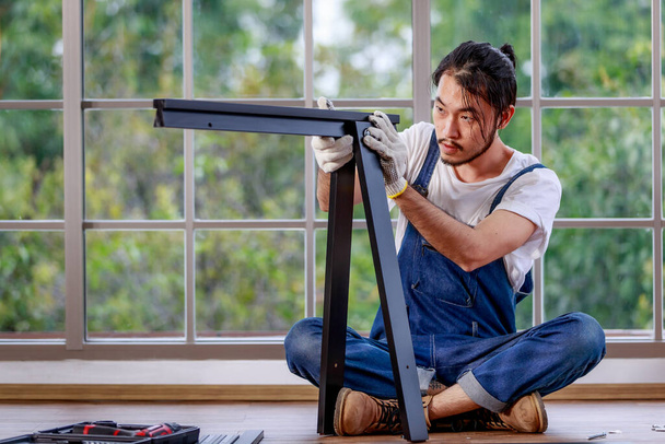 Fiatal hipszter ázsiai szakállas férfi dolgozik ezermester, összeszerelése fa asztal felszereléssel, koncepció otthoni diy, hobbi és önkiszolgáló, zöld fa a háttérben - Fotó, kép
