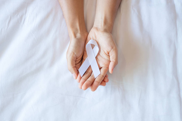 Novembre Mois de sensibilisation au cancer du poumon, démocratie et journée internationale de la paix. Homme tenant un ruban blanc sur fond blanc - Photo, image