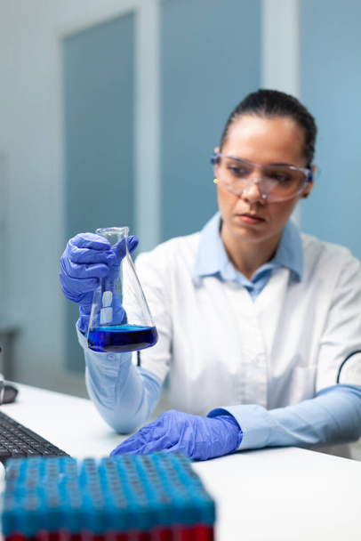 Médica cientista analisando artigos de vidro com solução azul desenvolvendo tratamento de saúde - Foto, Imagem