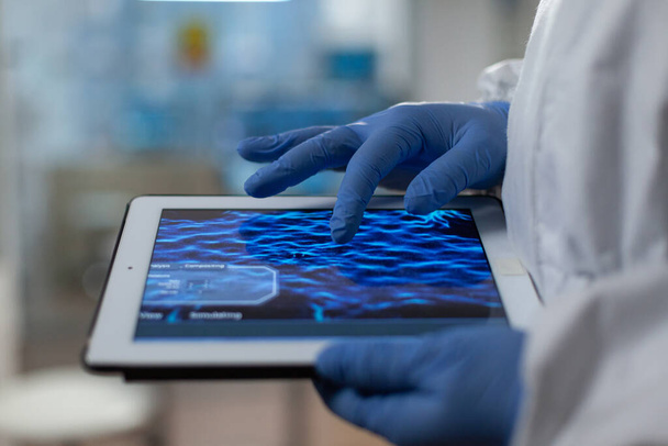 Médico cientista usando luvas médicas e ppe terno segurando tablet nas mãos - Foto, Imagem