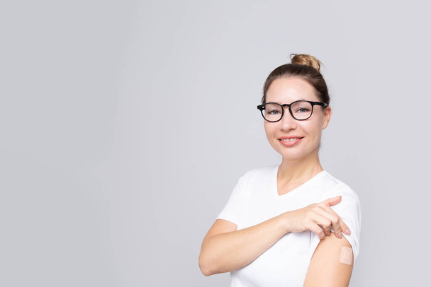 Woman and white T-shirt with a plaster on her hand rejoices from receiving a vaccination against coronavirus infection Covid-19. copy space. . - Foto, Imagem