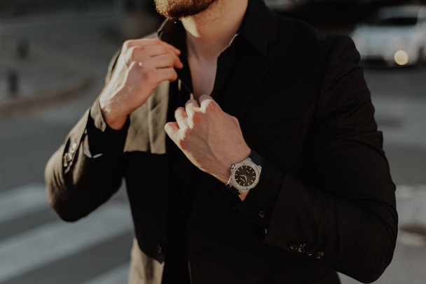 Un primo piano di un uomo d'affari attraente in un abito nero con un orologio costoso - Foto, immagini
