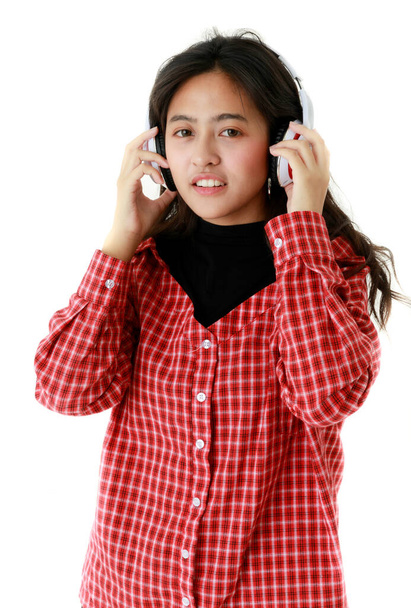 Мирная азиатка в крутом наряде слушает музыку в наушниках на белом фоне в студии. - Фото, изображение