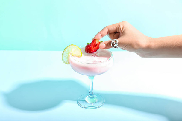 Woman decorating strawberry Pina Colada cocktail on color background - Фото, зображення