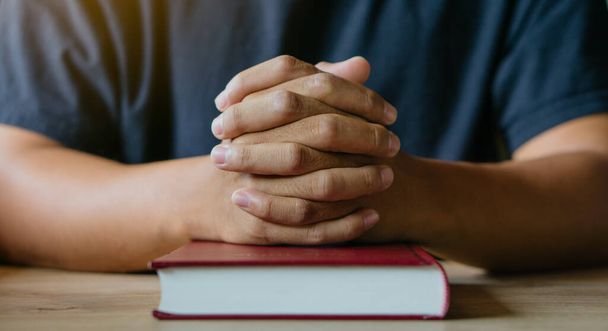 Hands of man with Bible praying.Christian life prayer to god. Man Pray for god.believe in goodness. Holding hands in prayer on a wooden table. - Photo, Image