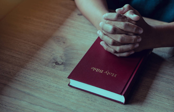 Hands of man with Bible praying.Christian life prayer to god. Man Pray for god.believe in goodness. Holding hands in prayer on a wooden table. - Photo, image
