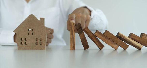 insurance with hands protect a house. The wooden domino block is about to fall on the house. Home insurance or house insurance concept - Photo, Image