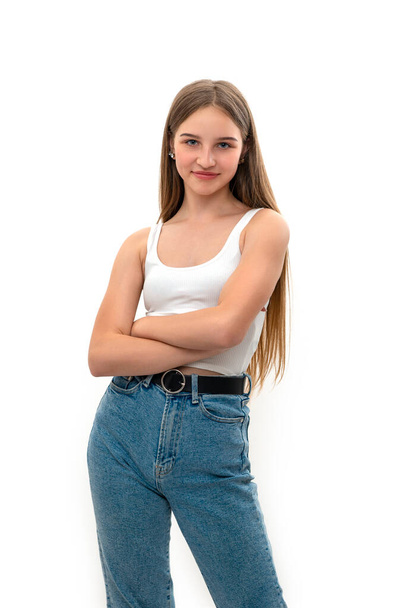  Puolipitkä muotokuva teini tyttö pitkät vaaleat raidat yllään farkut ja valkoinen toppi seisoo kädet ristissä valkoisella taustalla studiossa  - Valokuva, kuva