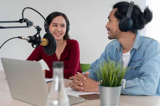 Ο Ασιάτης παρουσιαστής ραδιοφώνου Podcast στο στούντιο. Ένας άνδρας και μια γυναίκα ομιλητής μιλούν ζωντανά μέσω του Διαδικτύου με ένα κοινό στο σπίτι - Φωτογραφία, εικόνα