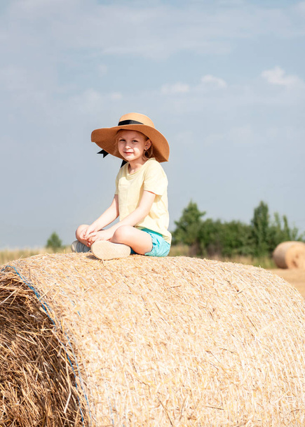 Little girl having fun in a wheat field on a summer day. Child playing at hay bale field during harvest time. - Foto, imagen