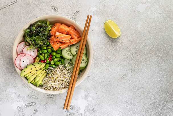 Healthy poke bowl with salmon, avocado, edamame beans, cucumber, radish, and seaweed, top view.  - Foto, Imagen