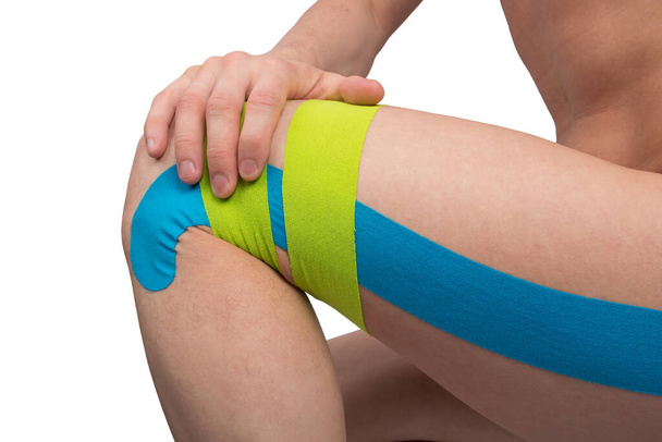 on a white background, the knee of the leg with glued kinesio tapes, to protect against injuries when playing sports - Foto, afbeelding