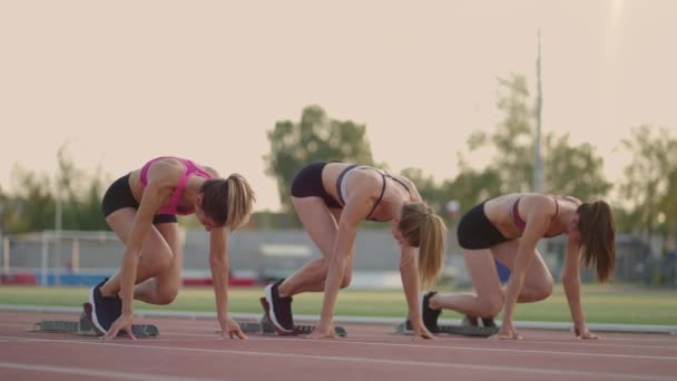 Τρεις νεαρές γυναίκες στο γήπεδο στη γραμμή εκκίνησης σε μπλοκ ξεκινούν στον αγώνα σε αργή κίνηση - Πλάνα, βίντεο