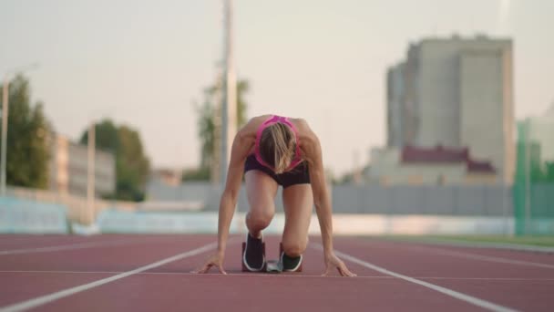 Női atléta futópályán kezdte a sprintelést. A futó elindul a futópálya rajtkockáiról. A fiatal női sportoló elkezd futni a háztömb elől. Lassú mozgás., - Felvétel, videó
