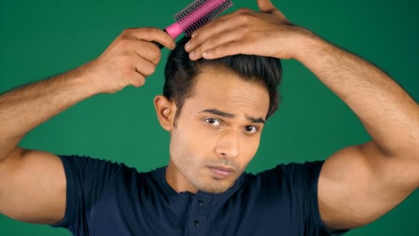 A college student combing and brushing his hair getting ready for a party. Handsome young man wearing a blue T-shirt styling his hair with a hairbrush - modern lifestyle, habit, party time, going out, social gatherings - Footage, Video