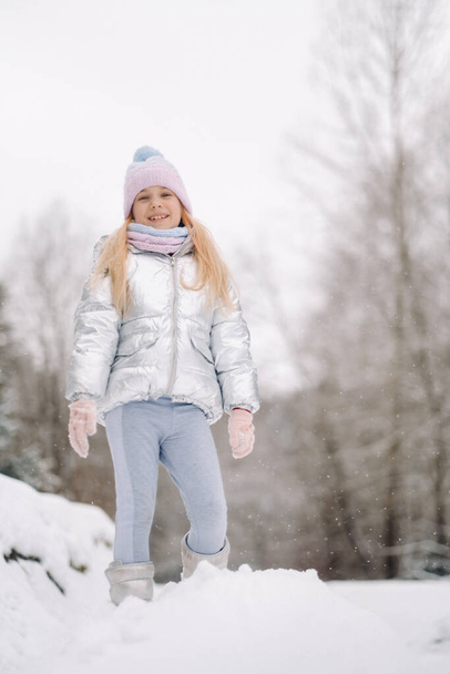 a little girl in a silver jacket in winter goes outside in winter. - Fotoğraf, Görsel