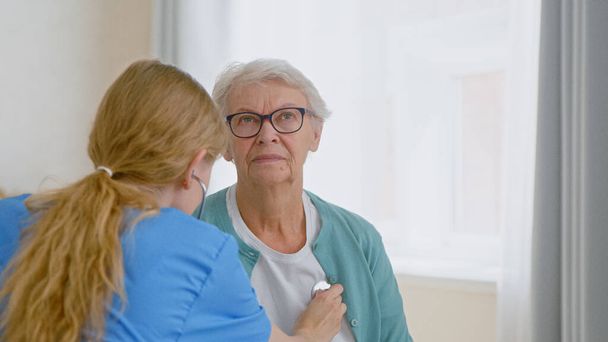 Yaşlı kadın hasta steteskopla muayene ediliyor ve doktor kalp atışlarını dinliyor. - Fotoğraf, Görsel