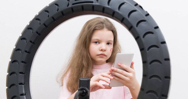 in the center of the circular lamp, a blogger girl with a heart on her cheek, holding a smartphone in her hand, close-up - Photo, Image